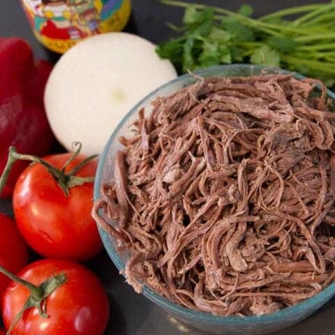 Glass bowl of shredded beef centered to the right and flanked by vegetables.