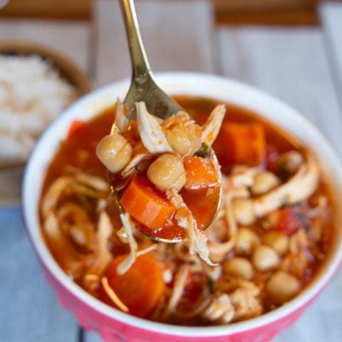 Bowl of chicken garbanzo bean soup with dish of white rice in the background.