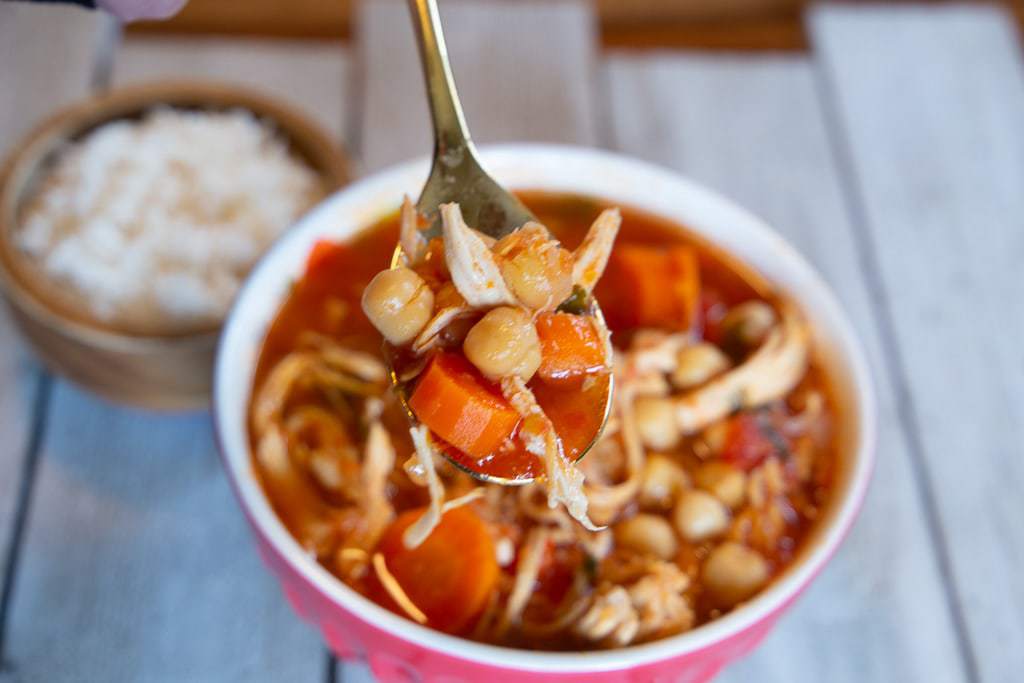 Bowl of chicken garbanzo bean soup with dish of white rice in the background.