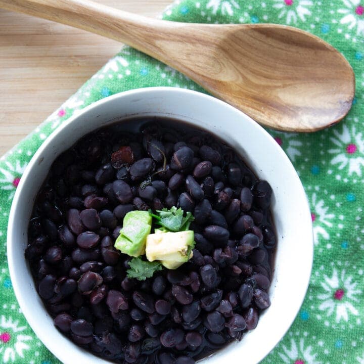 White ceramic bowl of Costa-Rican style slow cooked black beans topped with diced avocado and cilantro leaves.