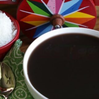 Black bean soup in a ceramic bowl beside a cloth napkin and spoon.