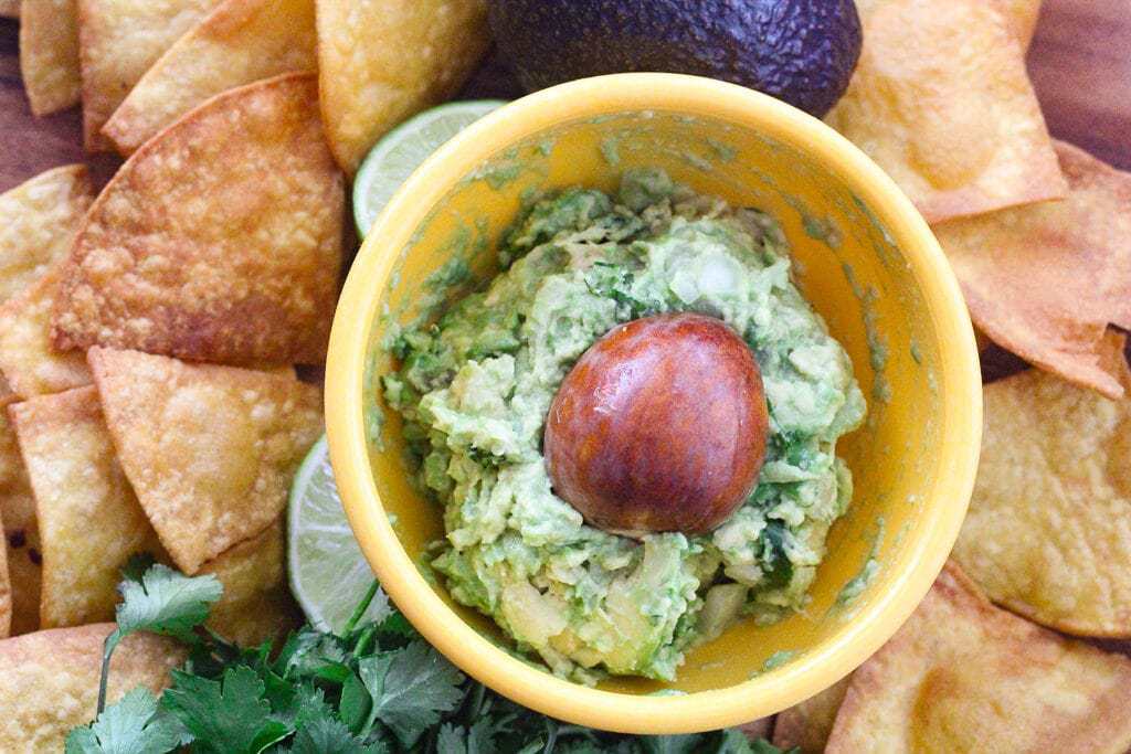 Yellow bowl of guacamole surrounded by tortilla chips.