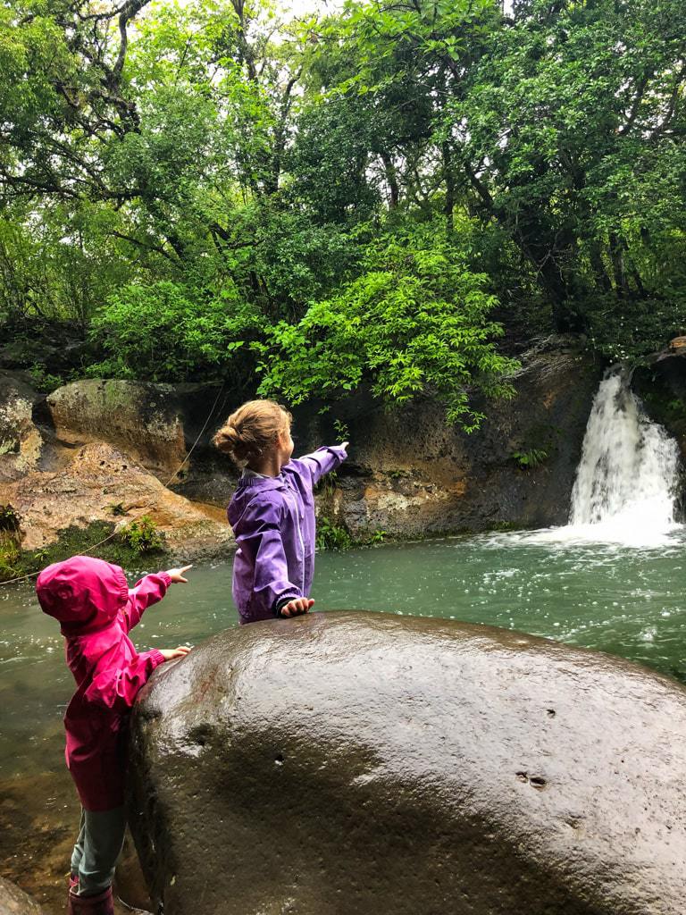 two young girls pointing to a costa rican waterfall in a rainstorm